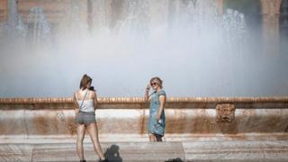 A woman take a photo of a friend in front of a fountain in Cordoba, Spain.