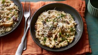 Two bowls of parmesan-scattered mushroom risotto sit on an orange cloth.