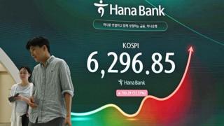A man and a woman walk past an electronic screen showing 31 July's Kospi trading figures