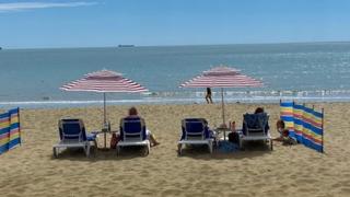 People sitting on sun loungers on a beach with sun umbrellas, blue sea and blue sky.