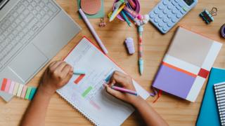 Top view of kid writing in a notebook on desk during studying at home - stock photo