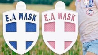 Two badges, one blue and one pink with a white cross and the words E A Mask at the top