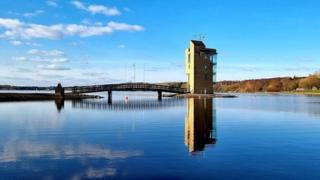 Blue sky reflected in the water which as a bridge leading to a building on an island