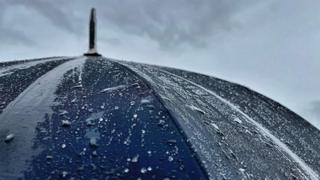 The top of an open black umbrella with rain bouncing off it