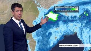 Chris Fawkes stands in front of a map showing potential rain accumulation over India.