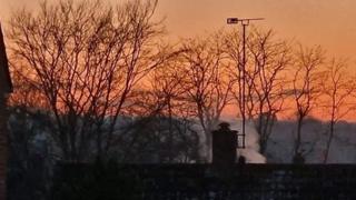 A red and orange sky behind silhouetted trees and roof tops