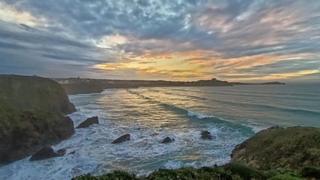 The sun setting over the sea at Porth, Cornwall, with yellow and blue sky reflected in the blue waterl