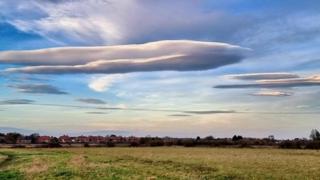 A huge flat cloud sits in a blue sky over a flat green field