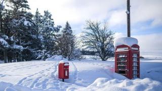 A red phone box and a red post box are covered in deep snow