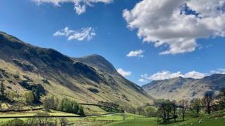 Bright blue sky with a few fluffy white clouds over a mountain in Cumbria.