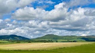 Bright blue cloud peaking through white clouds over mountains in the distance and fields in the foreground.