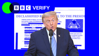 President Trump speaking in front of a microphone with a graphic showing a declassified document behind him.