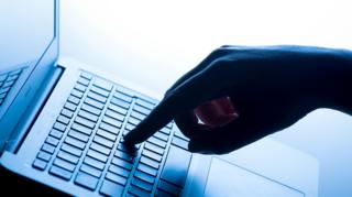 A close-up image shows a hand pressing keys on a laptop keyboard, with the computer screen out of focus in the background.