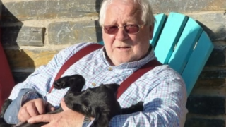 A man with grey hair and red glasses holding a small black dog 