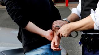 A young male with his hands behind his back as an officer puts him in handcuffs.