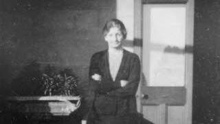 A black and white image of Mrs Pretty who has her arms crossed in front of her as she smiles at the camera