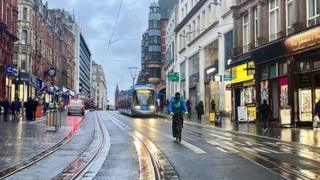 A cyclist and a tram come towards the screen down a wet Corporation Street, Birmingham