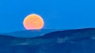 A large orange moon rising over the cliffs in the distance. The sea is rough with waves.
