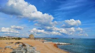 White clouds over a sandy beach and a flat blue sea