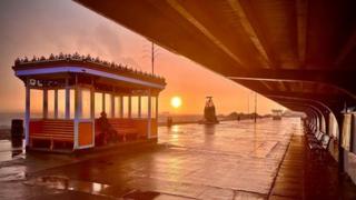 A man sits in a rain shelter beside the sea in Portsmouth