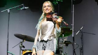 A blonde haired woman on stage playing a violin