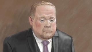 Courtroom sketch of Robert Bush in a dark three-piece suit standing alone against a plain brown background. He wears a light-coloured shirt and a purple tie. The illustration is rendered in soft pencil and pastel tones.