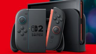 A black Nintendo Joycon controller and console displayed against a bright red background. The central panel has a Nintendo Switch logo with a large numeral 2 alongside it. One of the joycons is detached from the main joypad unit, showing a red connector trim.