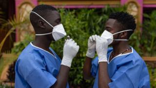 Two men wearing protective gear face each other while adjusting their masks
