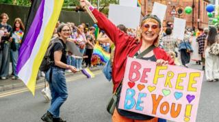 A woman is holding a colourful sign which reads: "Be Free Be You" as part of the Manchester Pride 2025 parade.