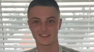 John Burns, standing in front of a window with open blinds, he is smiling and has shaved brown hair. 