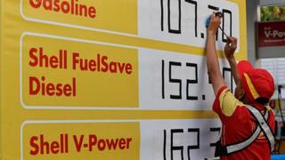 A worker at a Shell petrol station uses tape to change figures of fuel prices displayed on a board