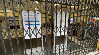 A London Underground station entrance is closed off with metal gates, with Transport for London signs behind them warning of disruption due to RMT strike action.