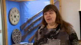 Anna NicChoinnich agus geansaidh dubh is glas oirre agus falt fada dorcha aice.