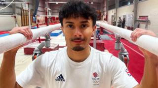 Jake Jarman standing between and holding parallel bars