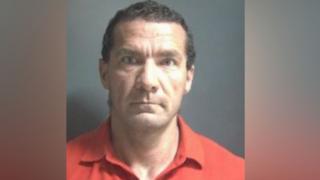 A police mugshot of Kovacs in an orange shirt