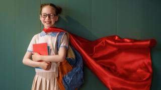 girl dressed up as a superhero holding books