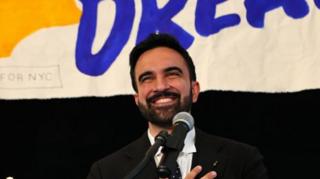 A photograph of Mr Mamdani on stage with a microphone in front of him 