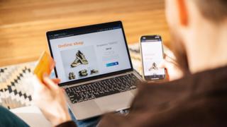 A man browses online using a laptop while at home to buy shoes.