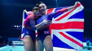 The Gadirova twins are dressed in red and blue leotards and holding the union flag behind them at the World Gymnastics Championship.
