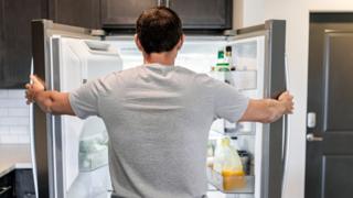 Back of hungry man opening fridge refrigerator doors domestic appliance searching for food inside with condiments and juice in modern kitchen - stock photo