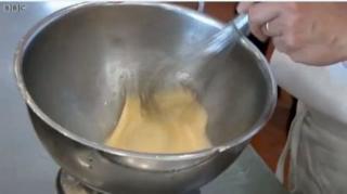 Picture of a silver whisk, whisking a cake mixture in a silver, metal bowl.