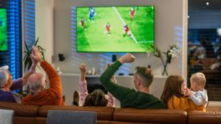 Excited Multigenerational Family Watching Football Match in Cozy Living Room - stock photo
