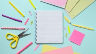 Notebook with a blank page and a lot of stationery items on a blue background. The concept of learning at school. View from above
