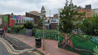 A Google Street image of a school behind a brick wall which has been painted green with pictures of leaves on it.