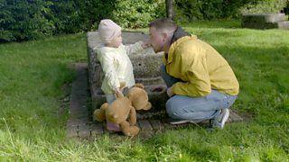 A dad talking to his toddler. He is crouched down, she is touching his nose.