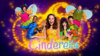 Cinderella wearing a yellow dress in front of a magical sparkling pumpkin. CBeebies House favourites surround her as part of the cast of CBeebies Panto 2025: Cinderella.