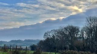 The sun glinting off a cloudy sky over a field