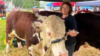 A woman with redish, brown hair standing next to a brown and white cow