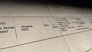 Close-up of an official UK death certificate from the General Register Office, showing typed details and headings, including registration district and cause of death, photographed under soft lighting.