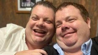 Two large men posing for the camera laughing and smiling. 